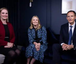 Three people seated in a studio with dark blue décor, facing the camera during a filmed panel discussion.
